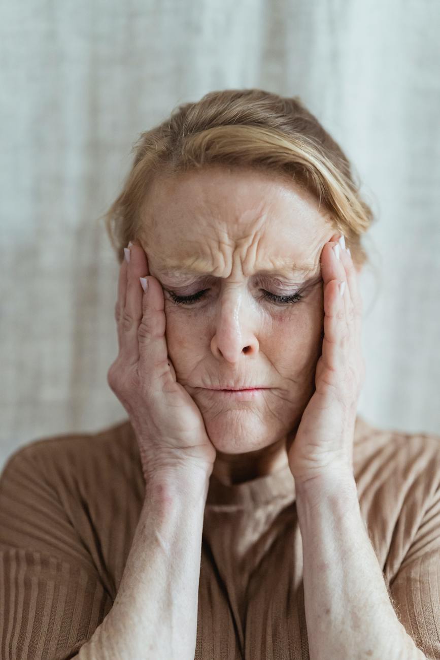 An older woman has her hands pressed to either side of her worried face.