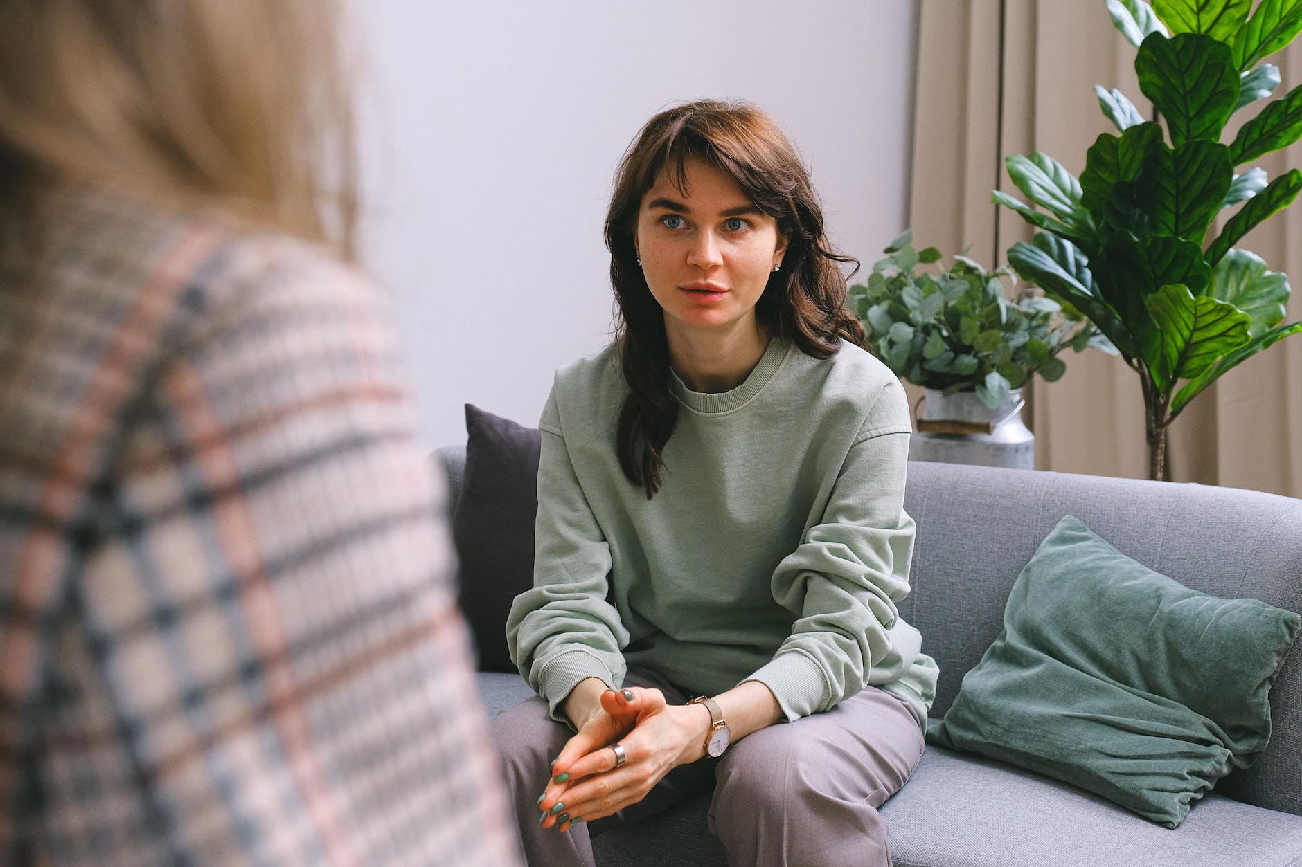 A woman is seated on a sofa facing another person. The woman is looking unsure or worried.