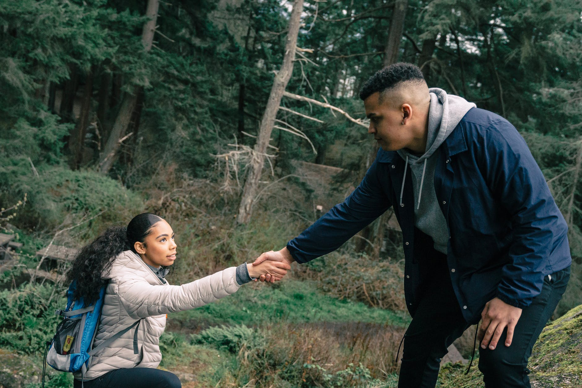 A couple hiking in the woods. A man is holding out his hand to help the woman up an incline.