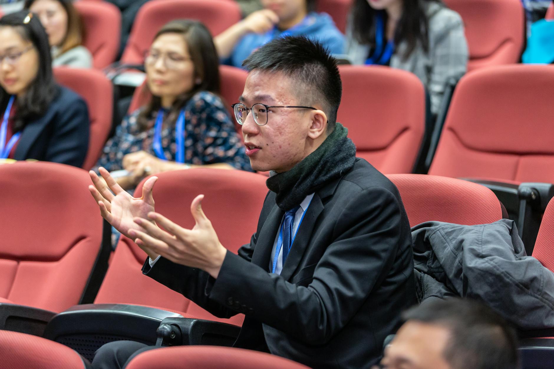 A student in a lecture hall expressively using his hand while commenting on the lesson.