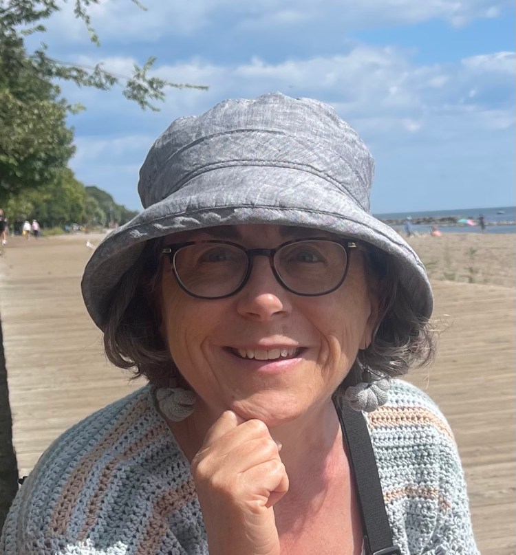 The author from the shoulders up wearing a sunhat smiling at the camera on the boardwalk at the beach.  