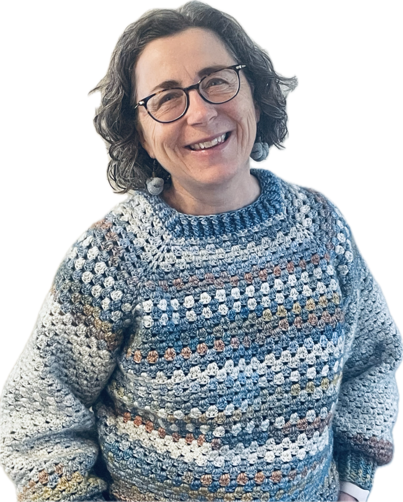 The author smiles while modelling a long sleaved, crew-necked crocheted sweater in shades of blue that she made.