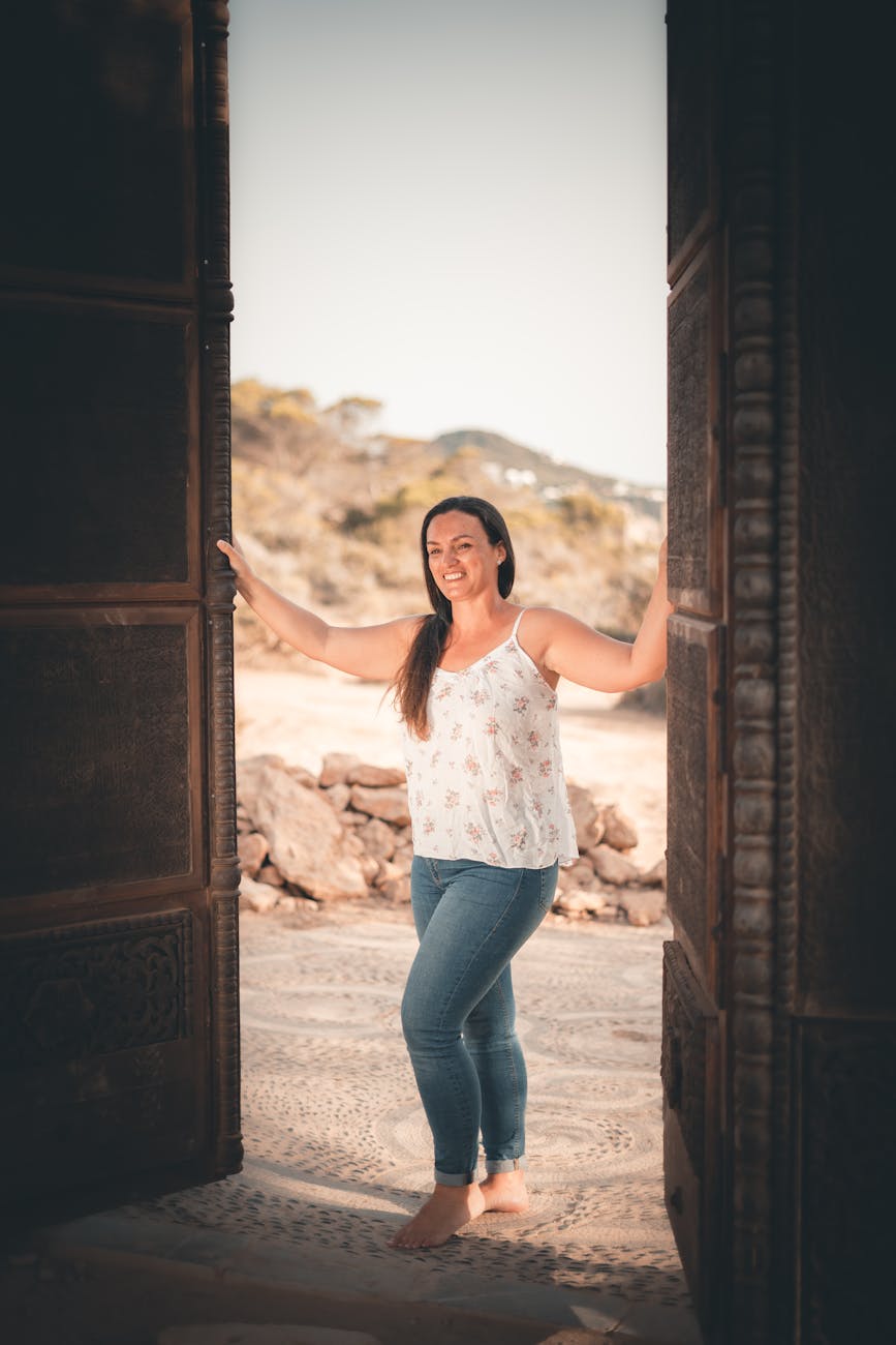 A woman opening two large wooden doors and smiling as she steps inside.