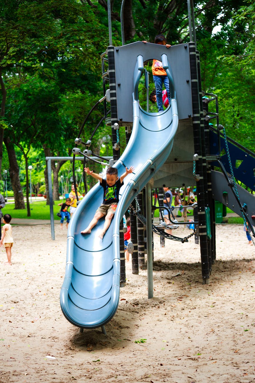 Children sliding down a plastic playground slide.