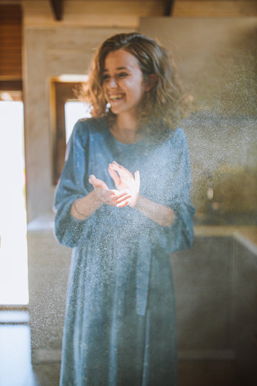 A woman in a blue dress stands in a ray of sunlight, smiling and clapping.