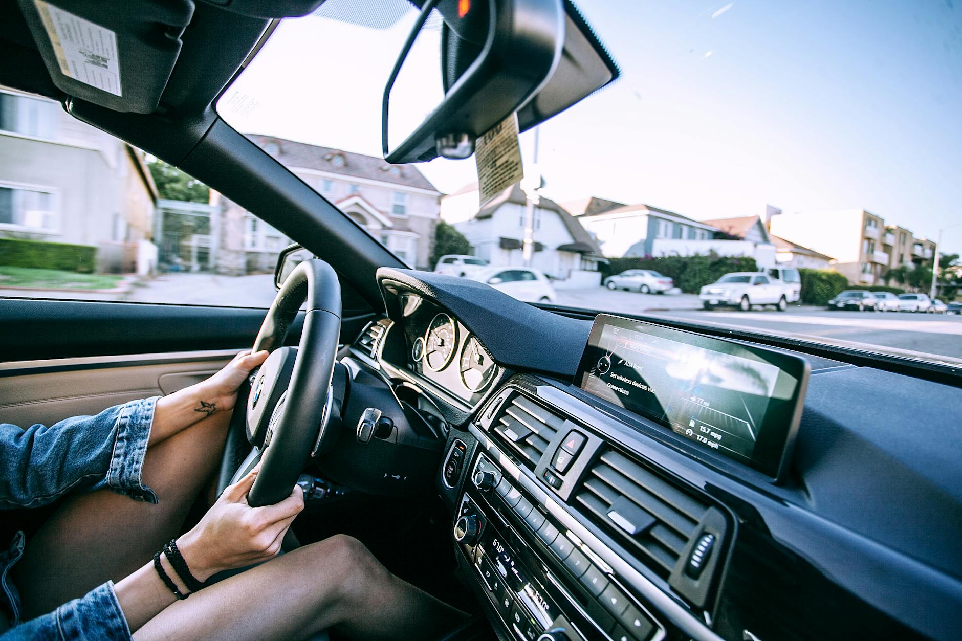 The interior of a car showing the dashboard and steering wheel while a person is driving through a residential neighbourhood.