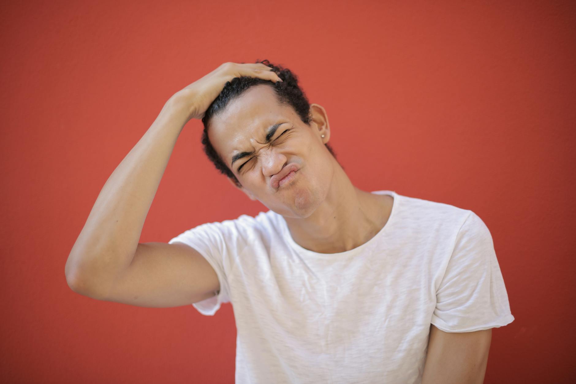 A person holds their head to one side while pulling an awkward expression by scrunching up their eyes and nose.