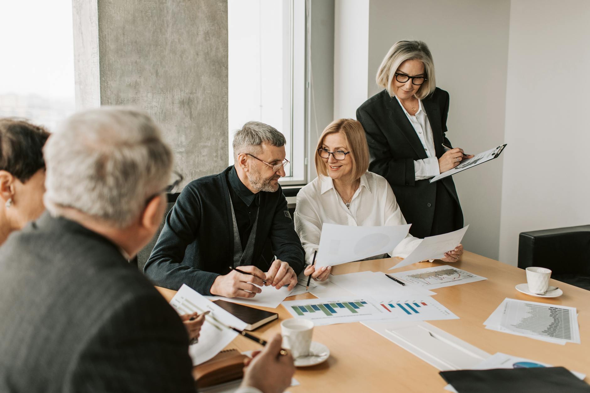Five coworkers sit around a table looking at graphs on papers scattered across the table.