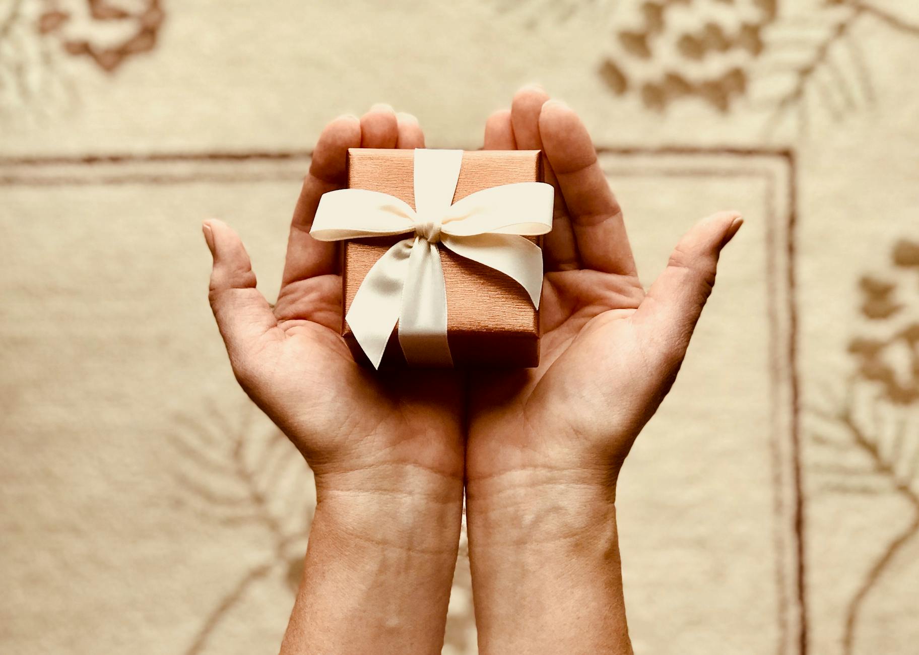 Hands hold a small gift box wrapped with a golden bow.