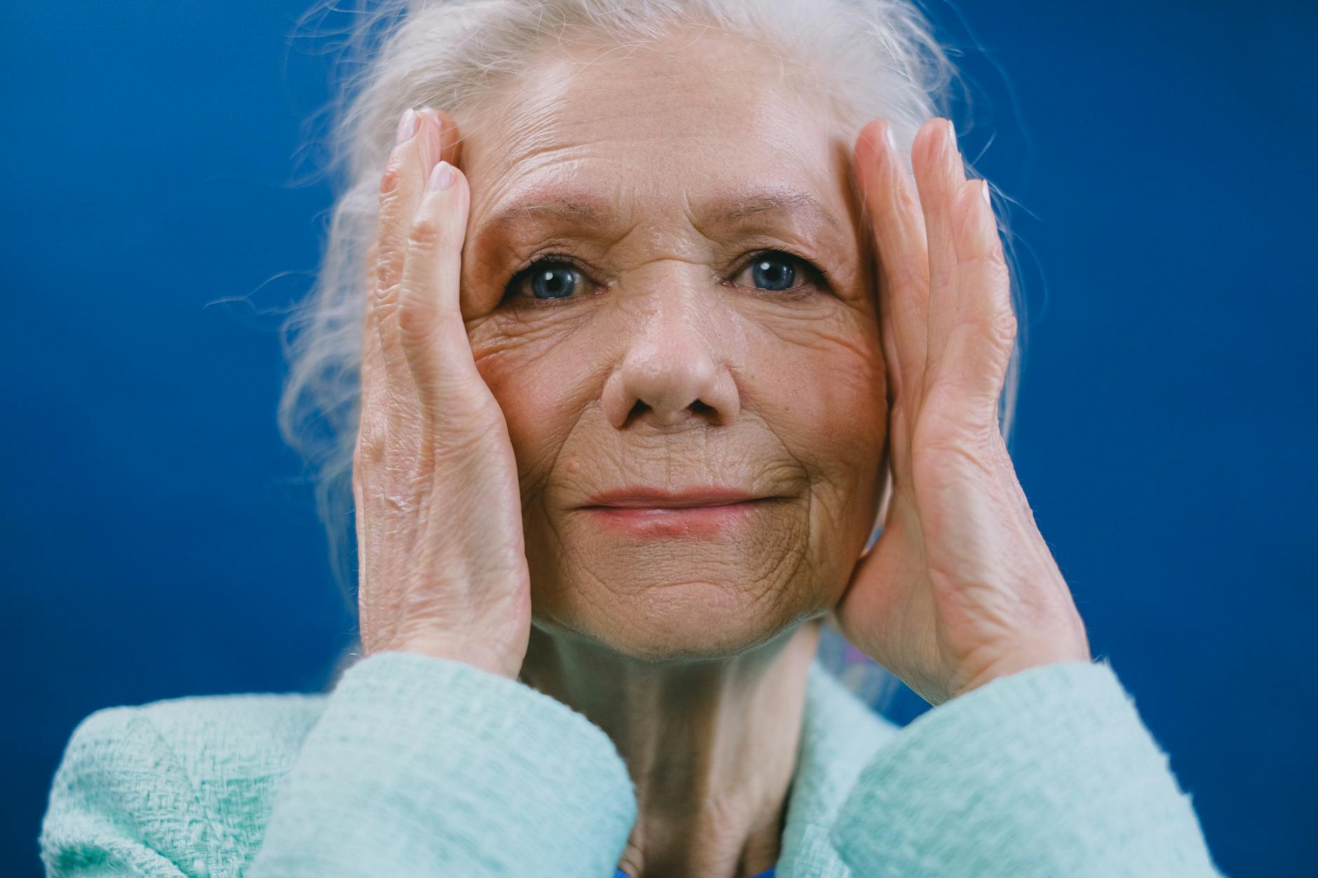 An older woman holding the sides of her face and staring ahead in overwhelm.