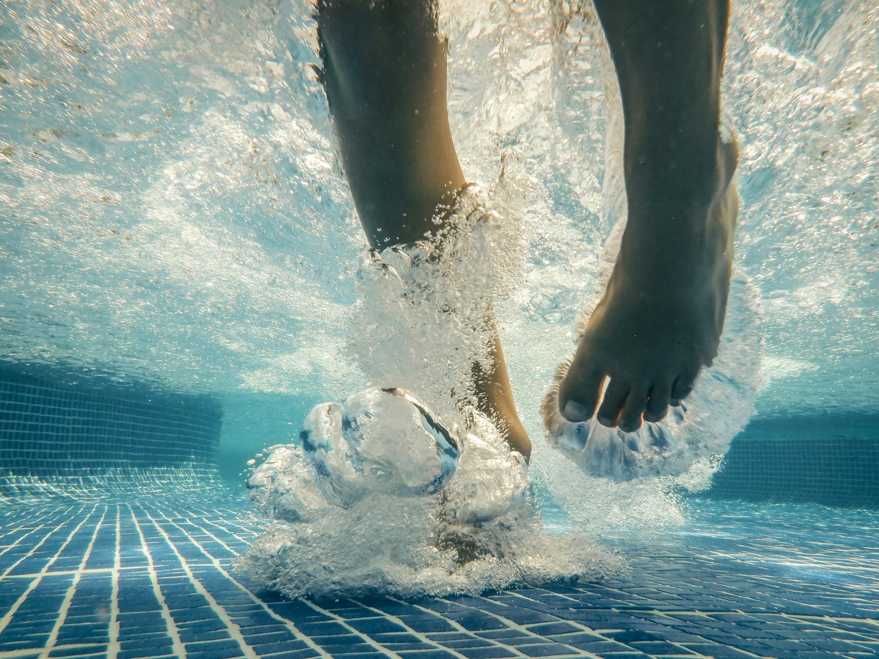 Feet in a swimming pool just touching the blue tiled bottom.