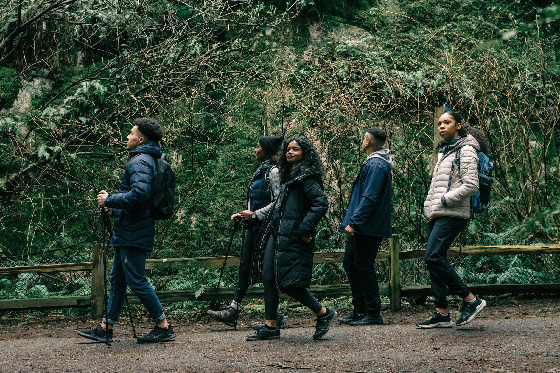 Five people in warm coats hike along a trail. Some carry backpacks and some have hiking poles.