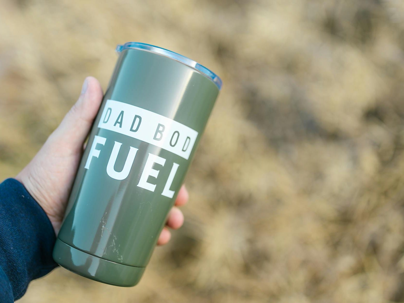 A person is holding a travel mug with the words, "Dad bod fuel," on it in white lettering.
