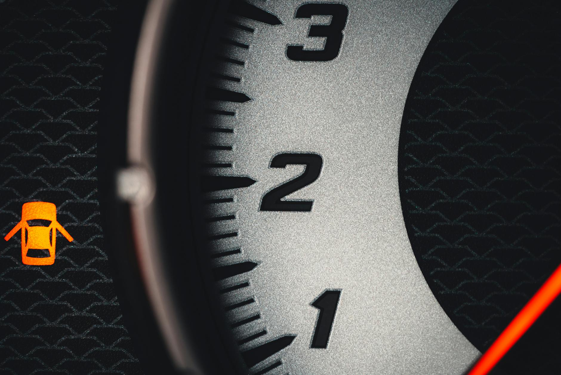 On a dashboard, a close-up of the numbers 1,2,3 on a speedometer and the red open doors warning light.