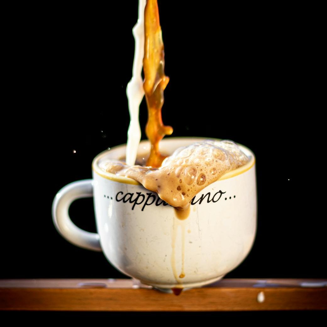 A coffee cup is being over-filled with espresso and milk.