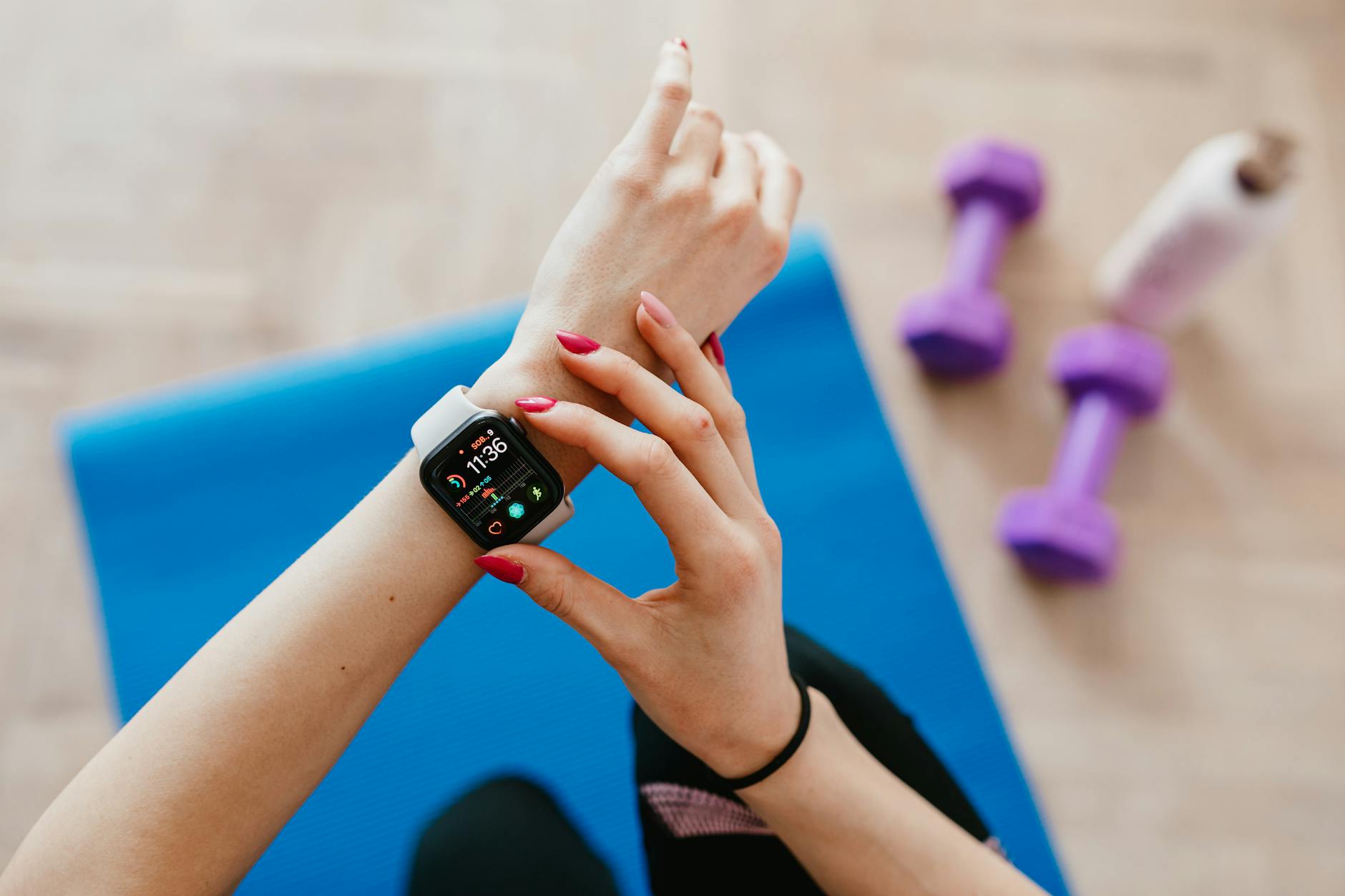 A woman's hands with red nail polish checking her fitbit watch at the gym.