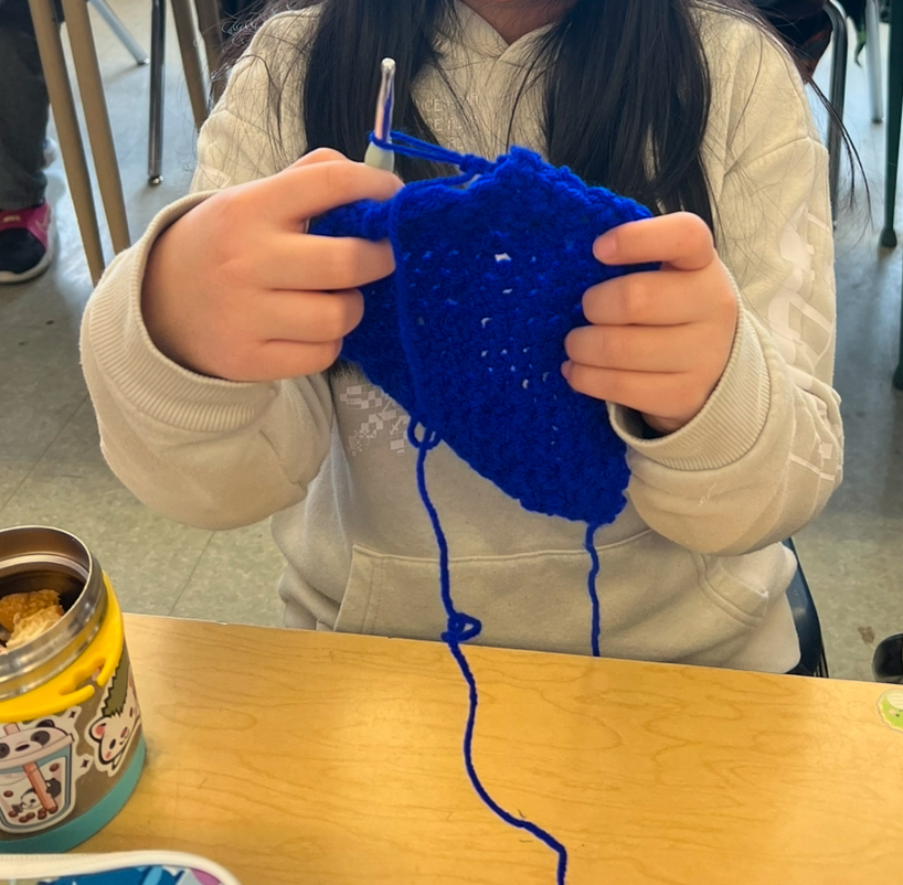 Three students hold up their crochet projects.