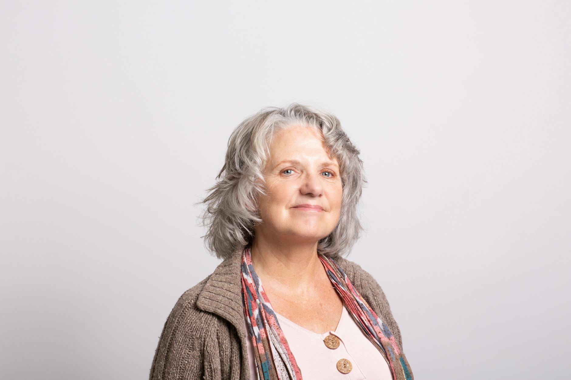 A woman with shoulder length grey styled grey hair smile confidently at the camera.