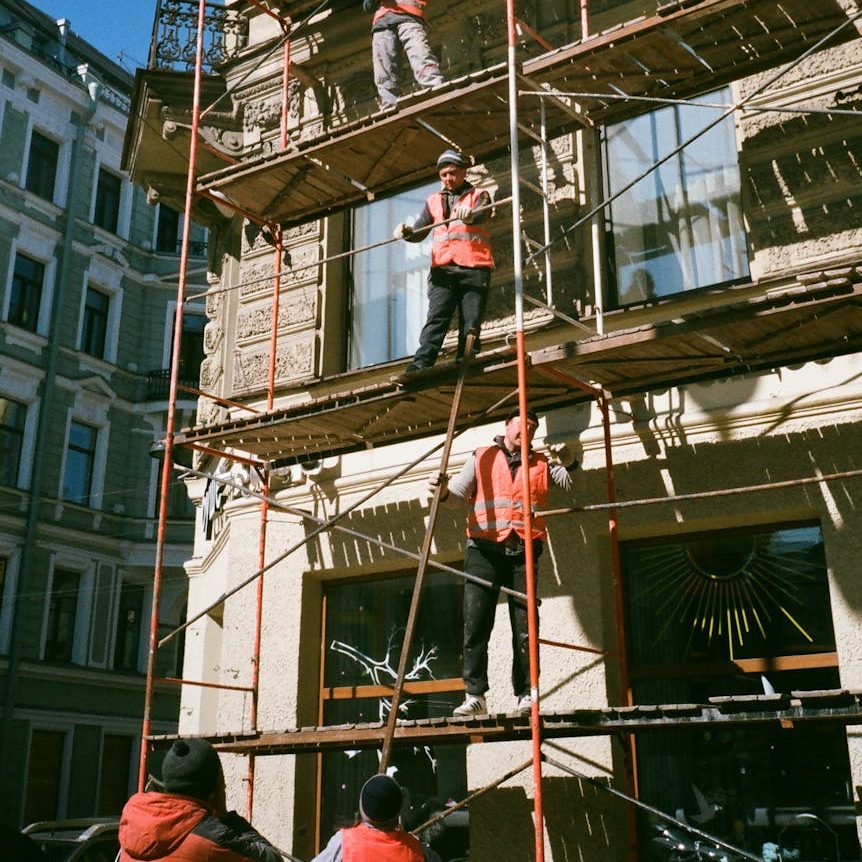 Three construction workers on scaffolding outside an older multi-story building.