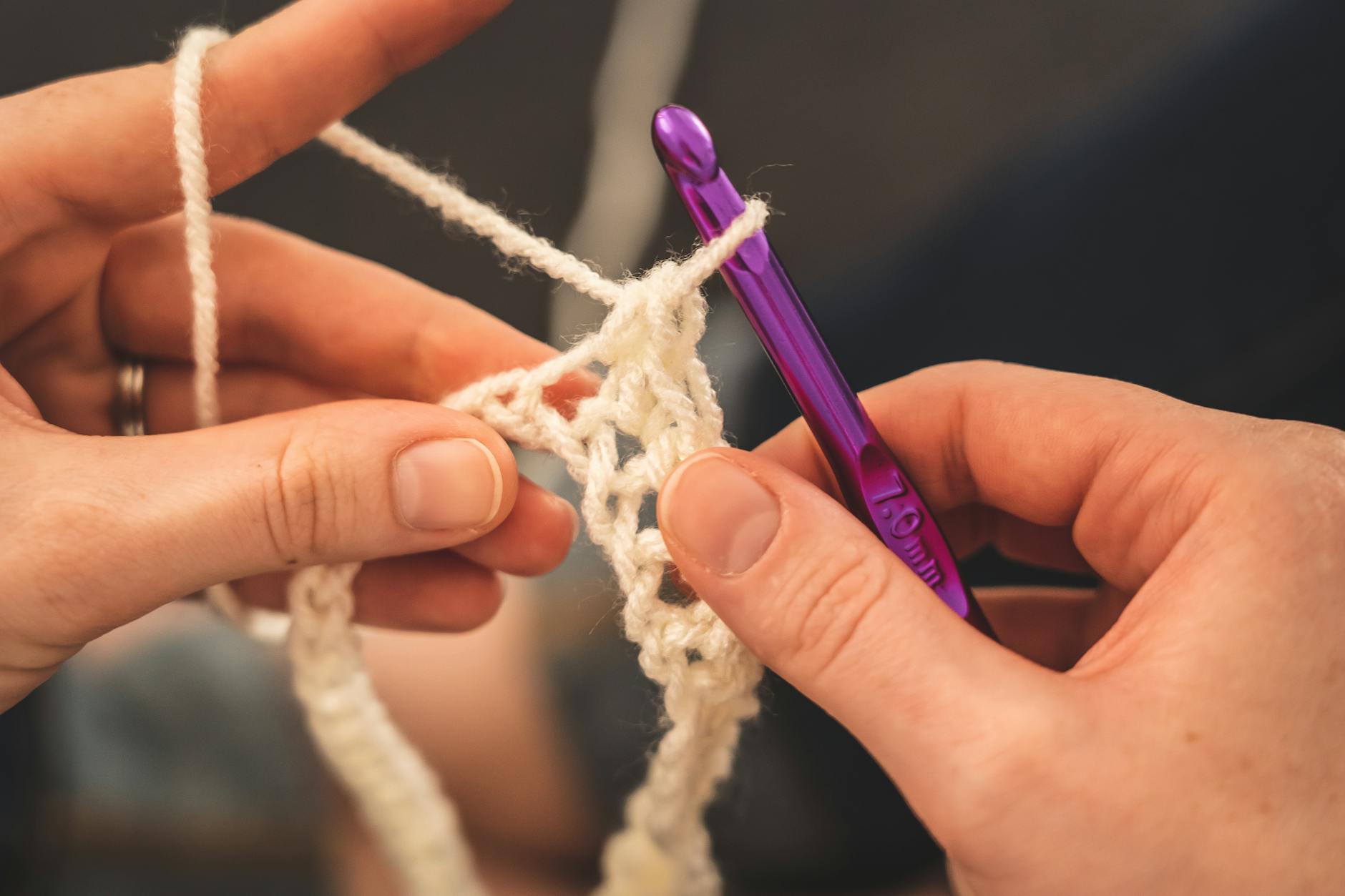 Hands hold cream-coloured yarn and a purple crochet hook while making single crochet stitches.