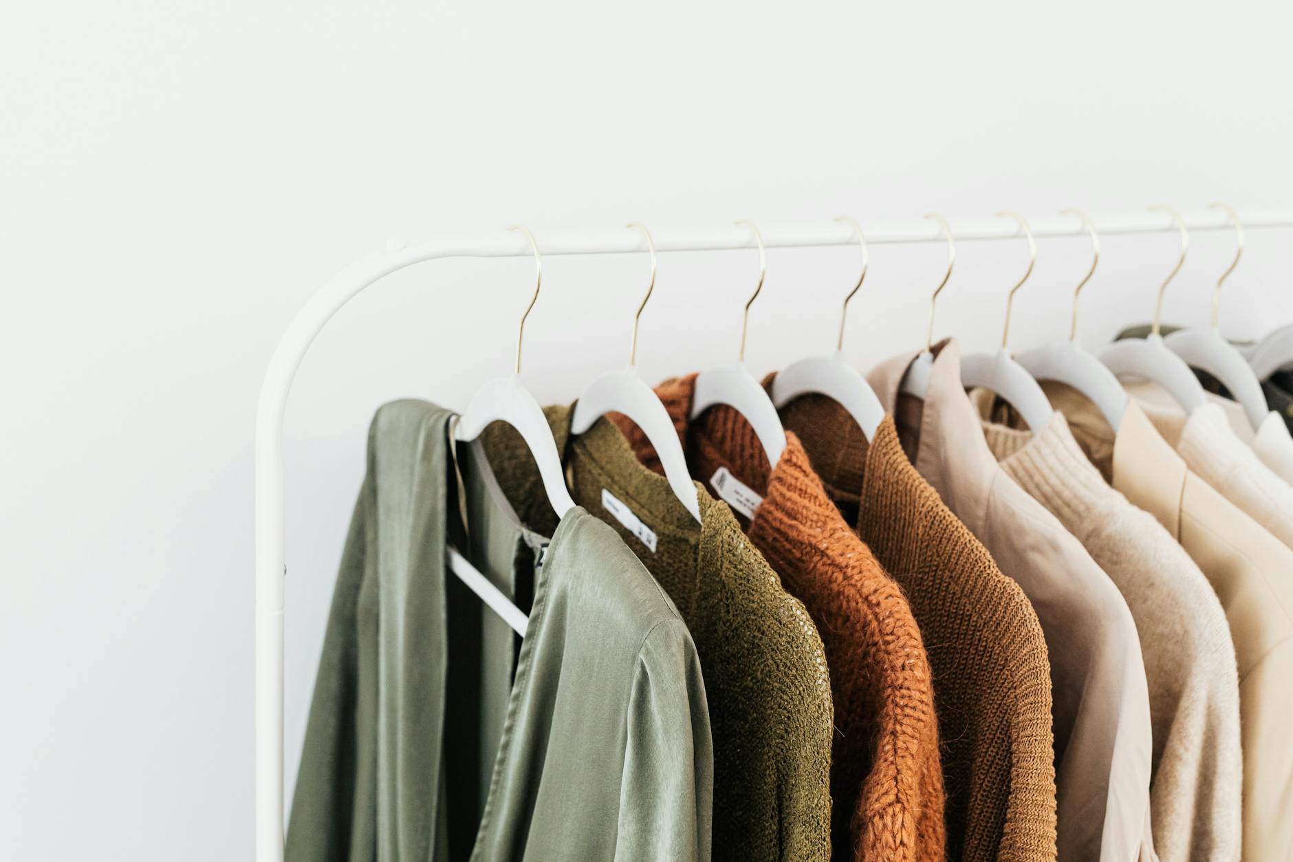 A variety of green, and neutral clothes on hangers on a clothing rack.