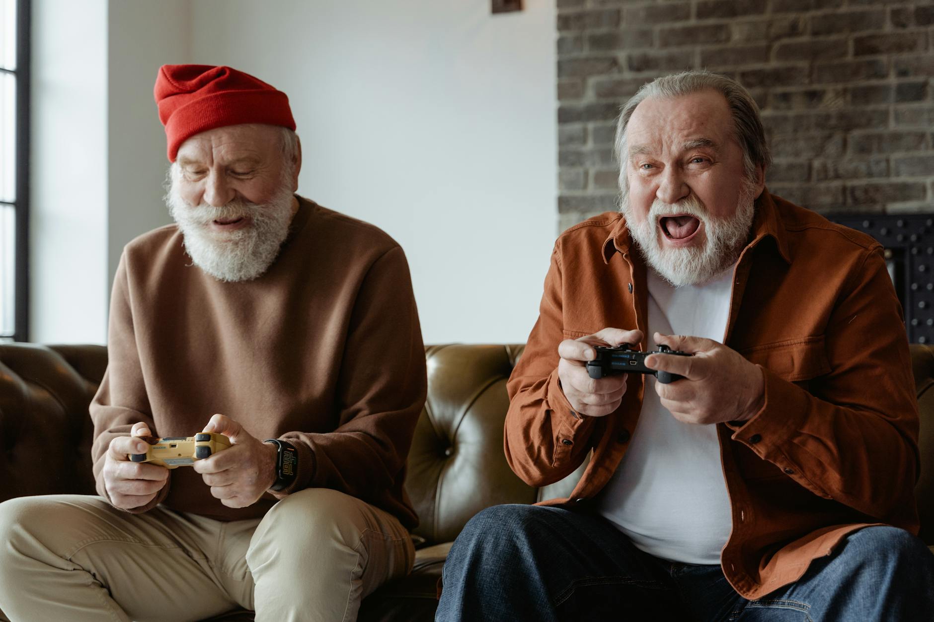 Two older men sit side by side excitedly playing video games. 