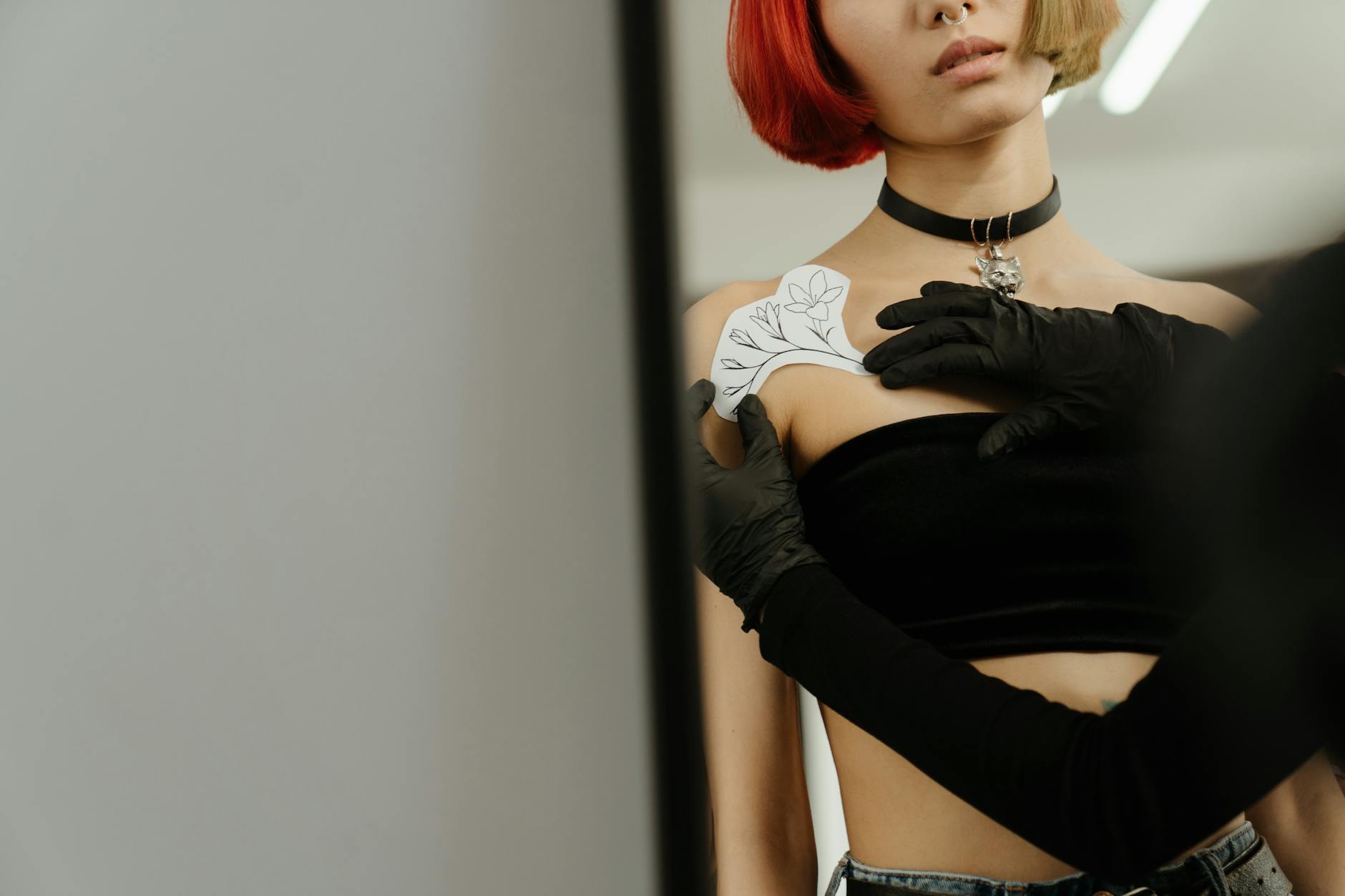 A tattoo artist is positioning the paper version of the floral tattoo design against a woman's shoulder.