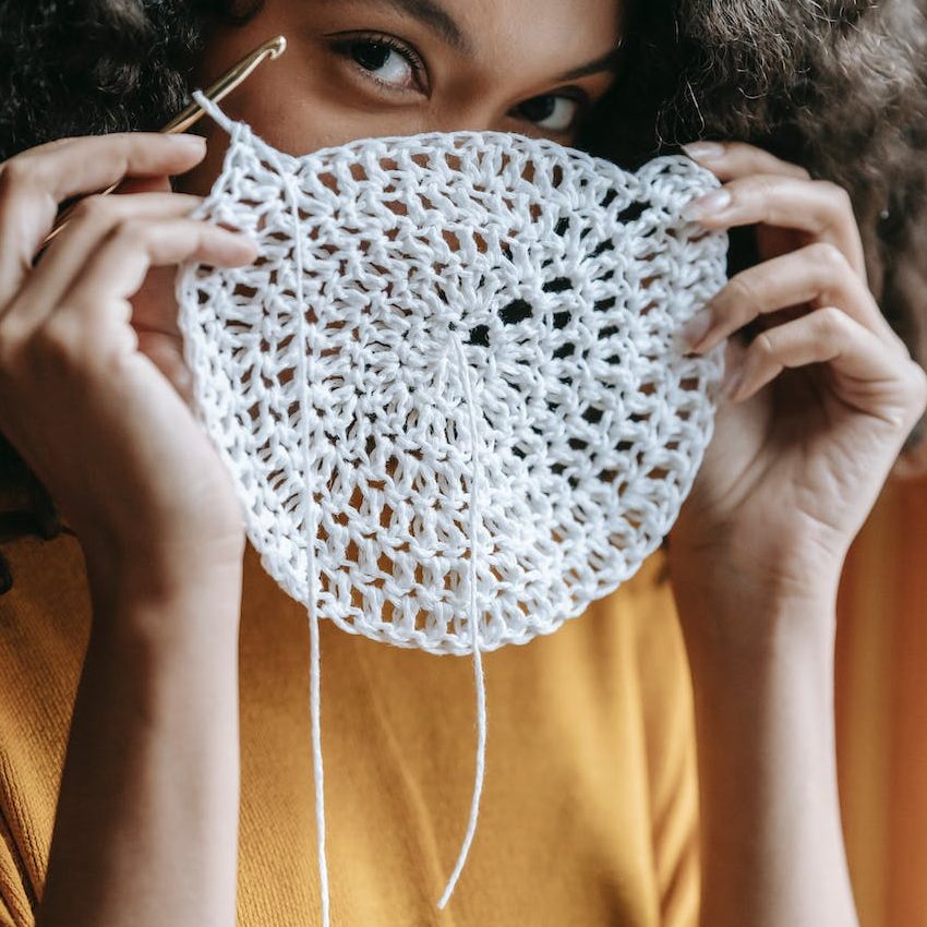 A woman is looking over the white crocheted circle that she is holding up.
