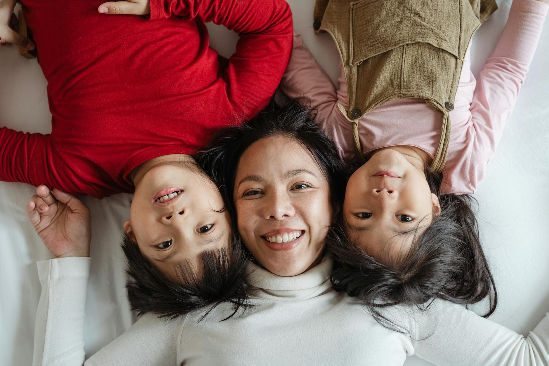 An overhead shot of a mom and two kids. The Mom is right side up and the kids are upside down on either side of her.