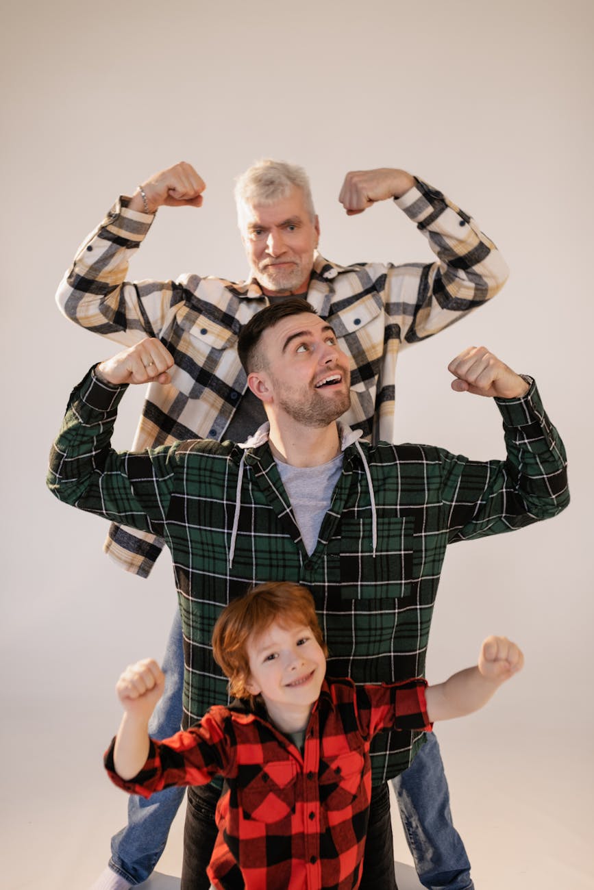 Three generations of males (senior, younger adult, boy) are holding their arms up to show strength.