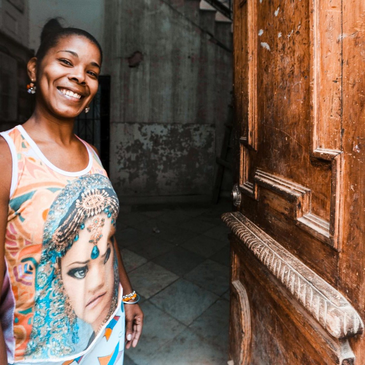 A woman smiles welcoming someone at an open old wooden door.