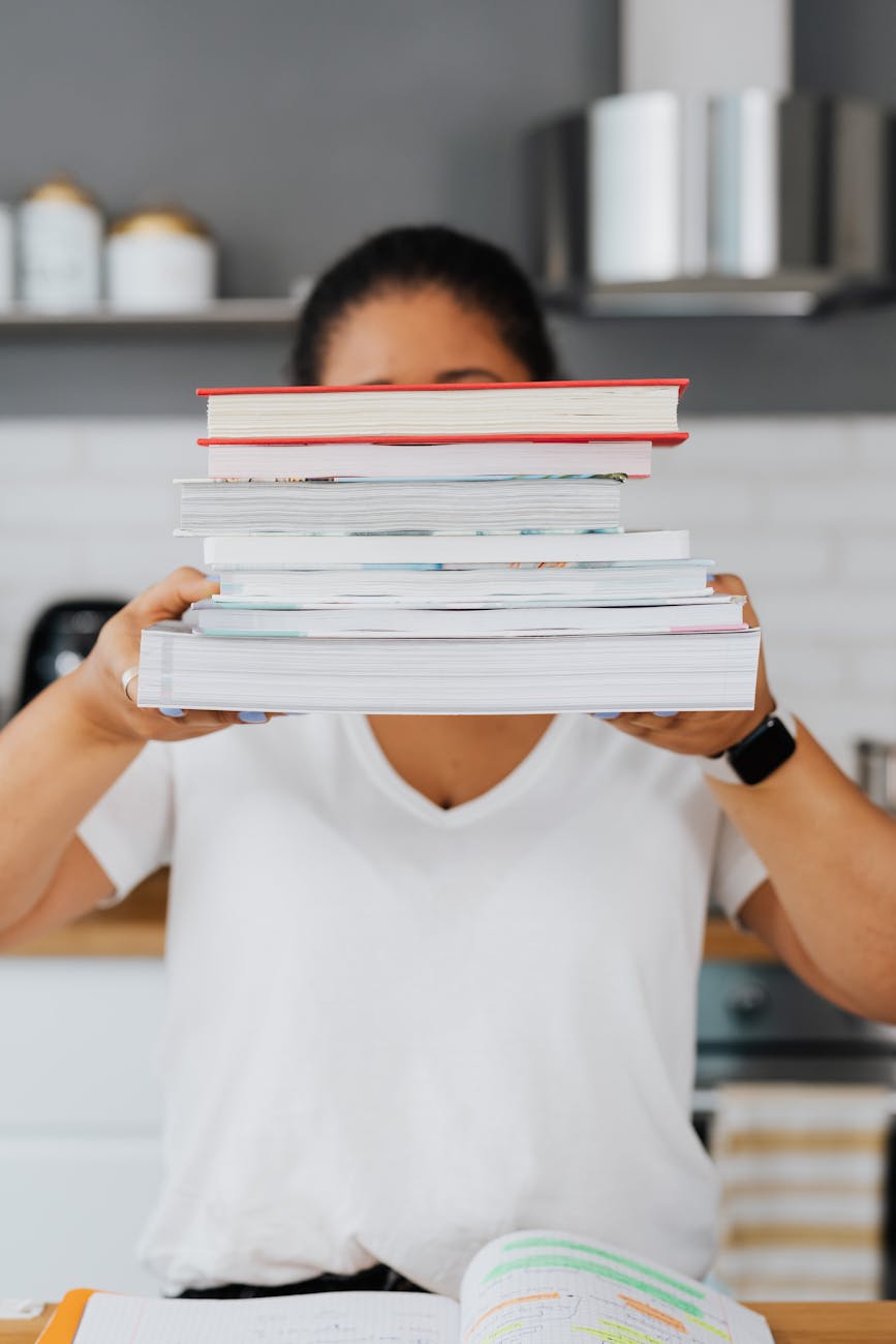 A woman holding a stack of books in front of her face.