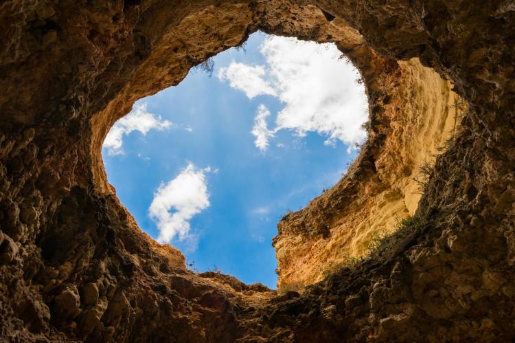 Looking up at a blue sky with clouds from the bottom of a pit.