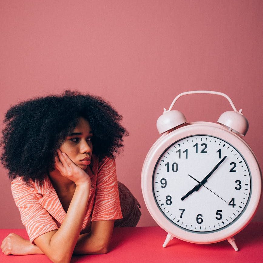 A person looks with a worried expression at a very large pink alarm clock.
