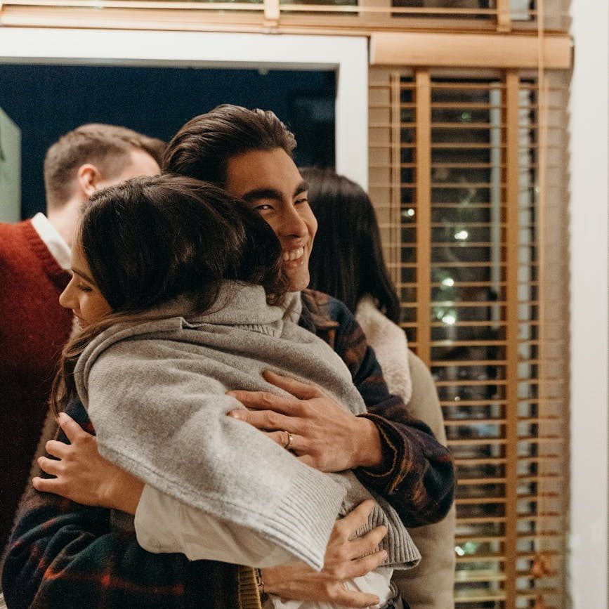 Friends smile and hug each other at the entrance of a home.