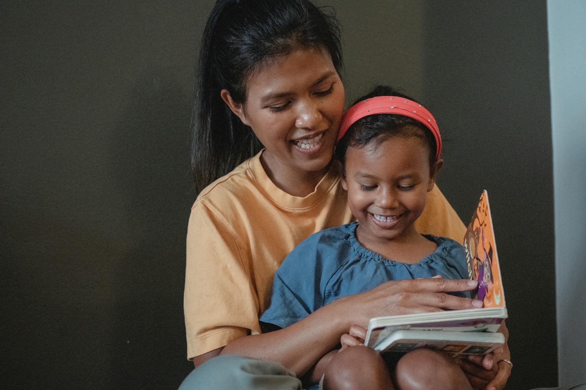 A woman reading to a child who is sitting on her knee.