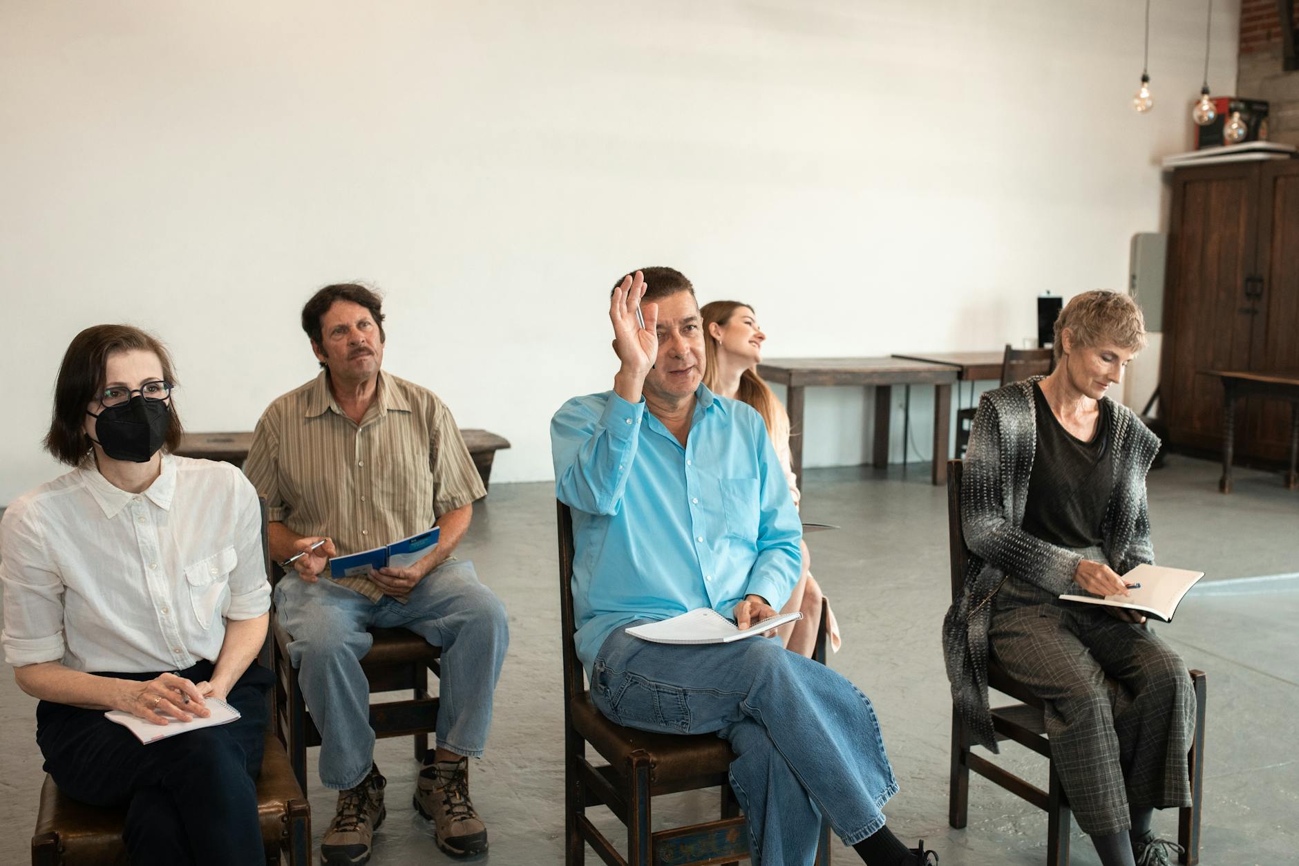 Adults sit in a small class with notes on their laps. One man raises his hand.