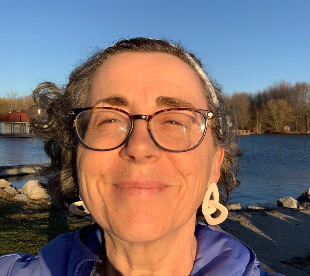 The author smiling into the sunshine with a lake and blue sky behind her.