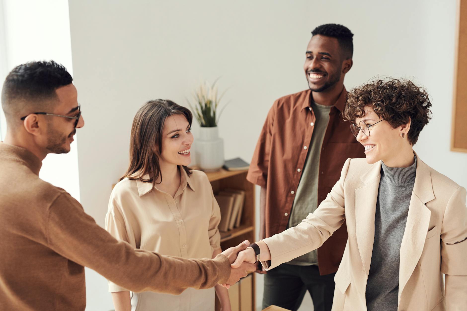 Four smiling people gathered together with two of them shaking hands.