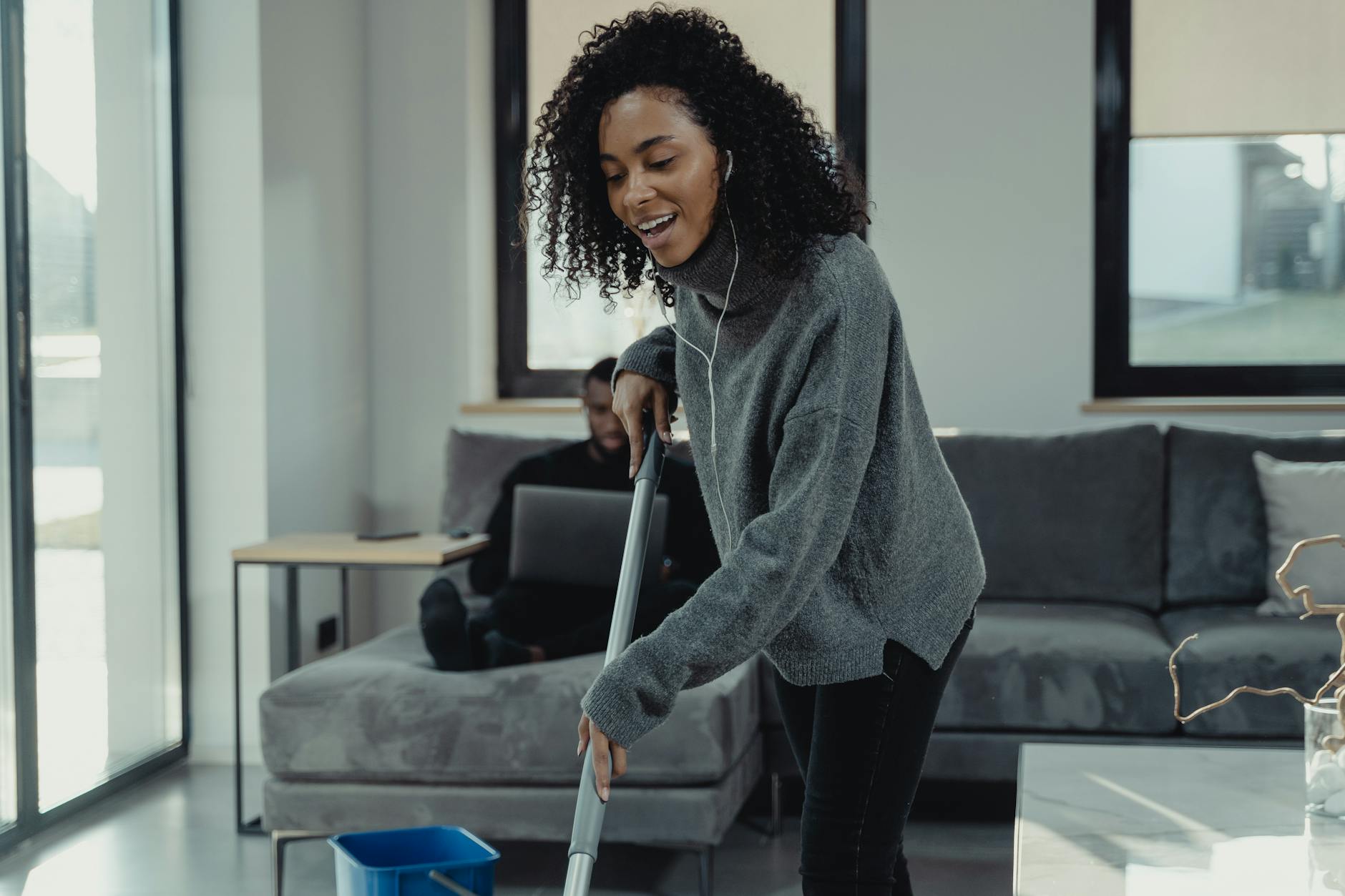 A woman is listening on headphones while mopping the floor.