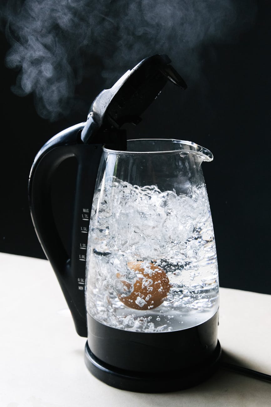 A clear-sided electric kettle of boiling water sits with it's lid open on a table.