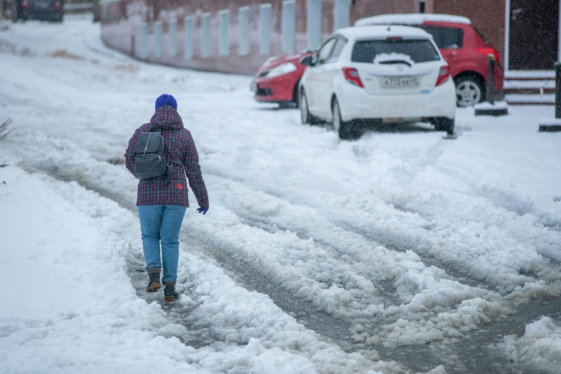 A person in winter clothes with a backpack walks away through a street covered in icy slush.