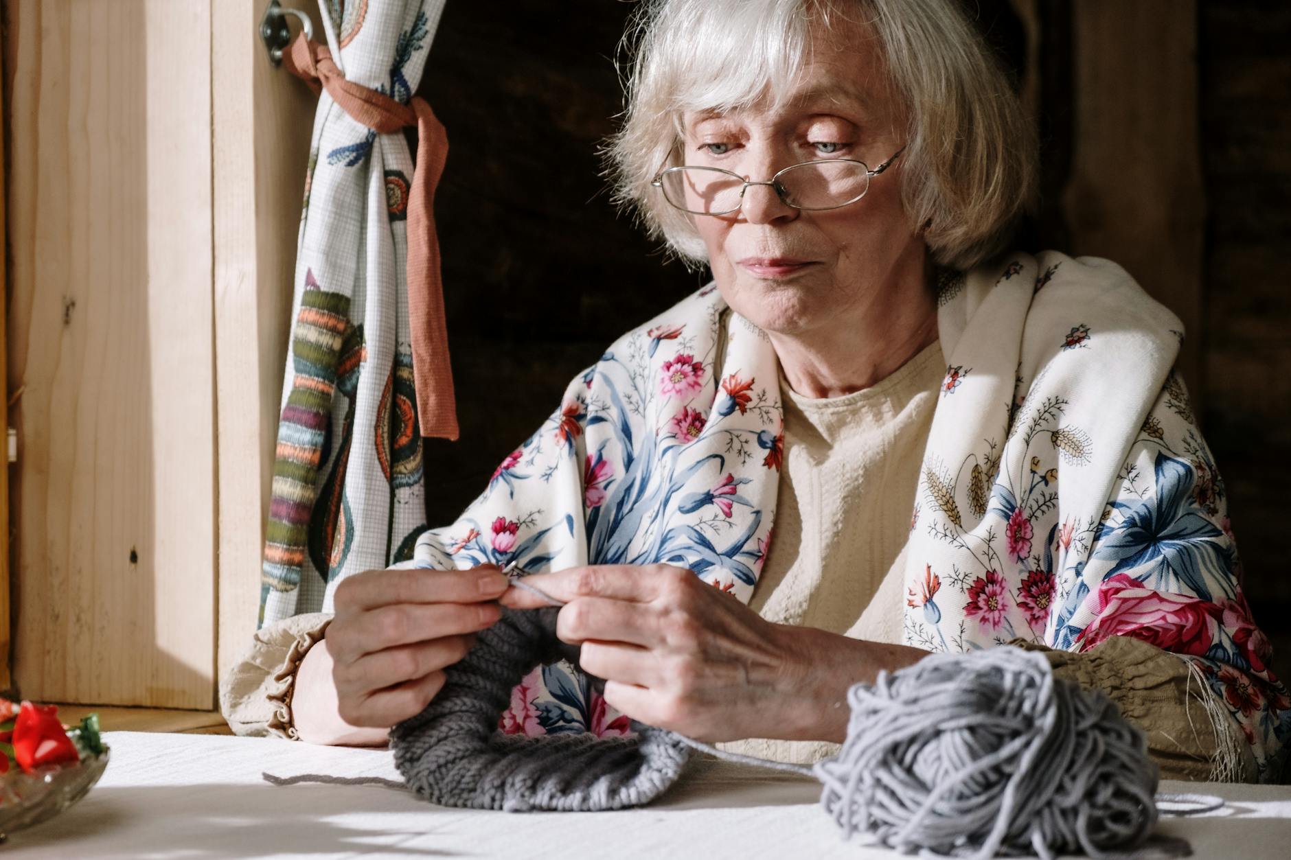 A woman uses circular needles to knit ribbing in grey yarn.