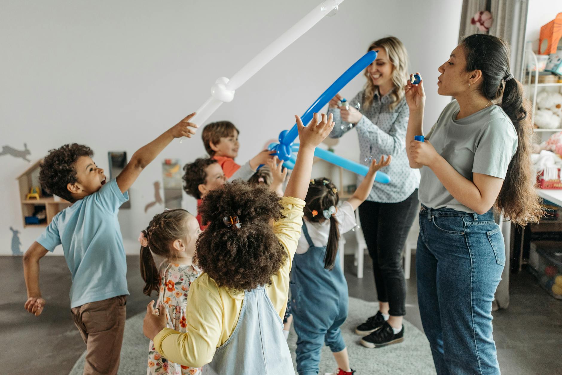 Two teachers work together with a group of active young children playing with balloon swords and bubbles.