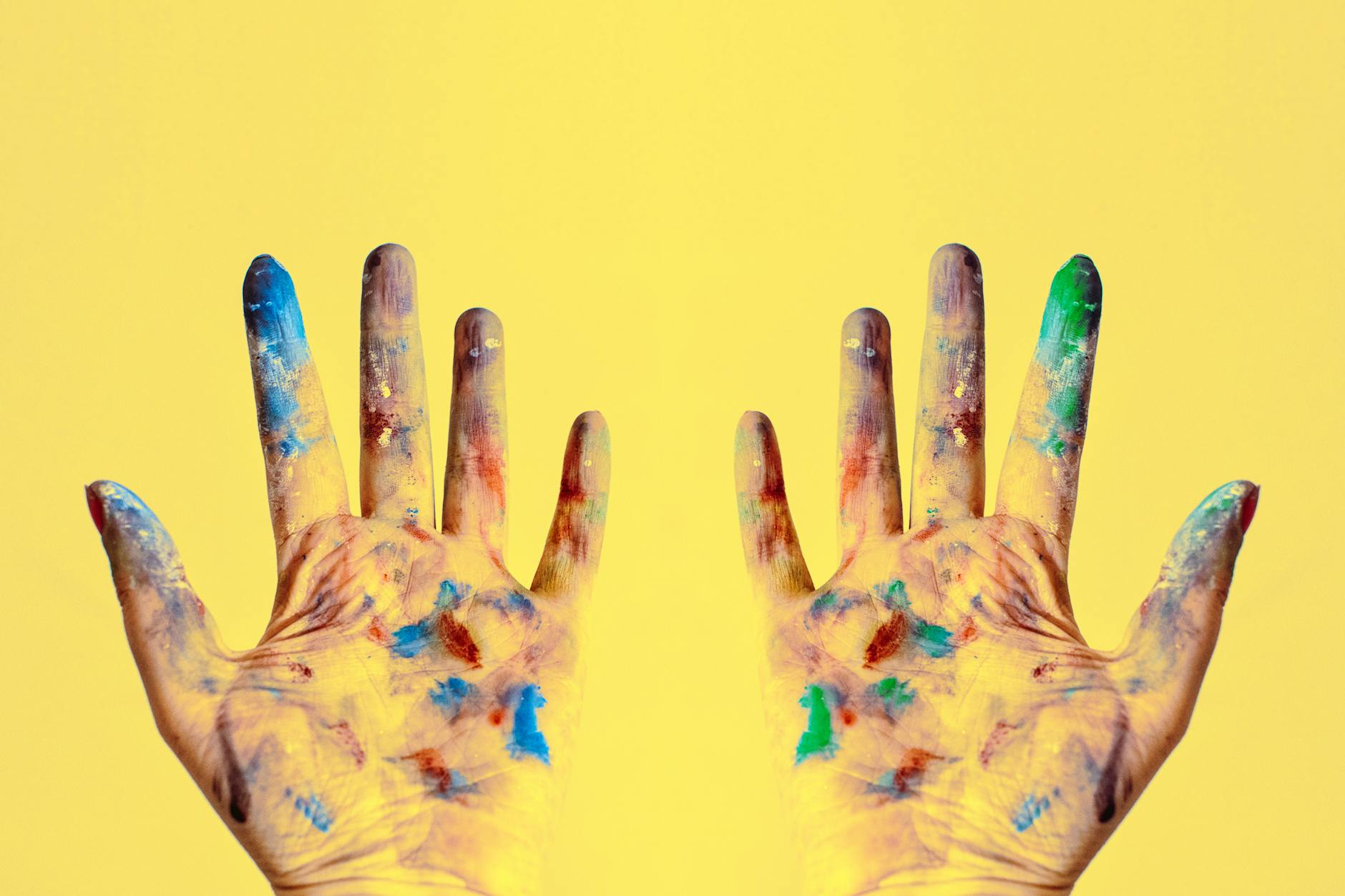 Two hands with the palms covered different dabs of paint. 