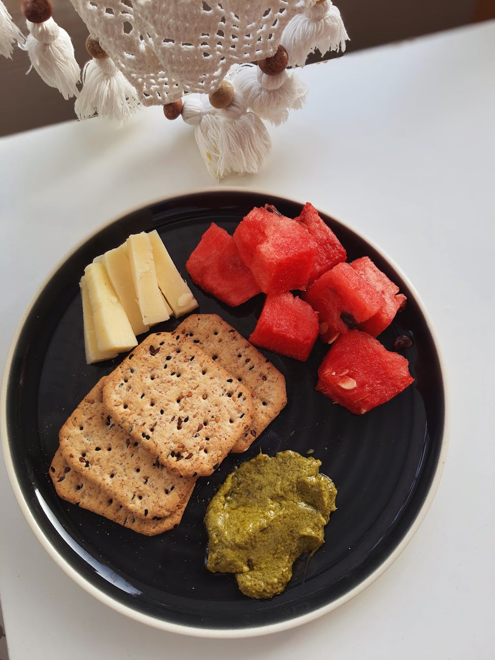 A plate with crackers, cheese, watermelon and spread.