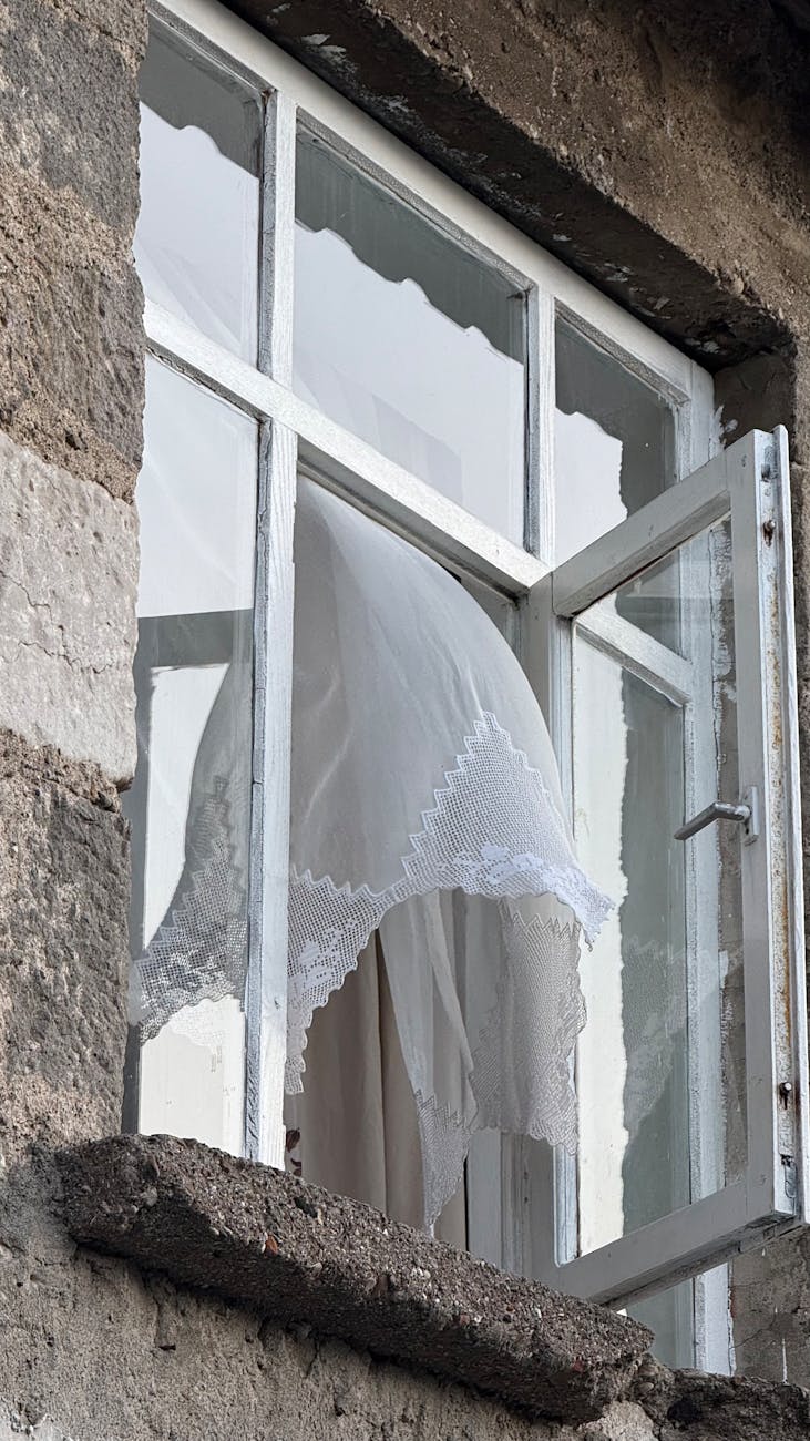 An open window with a white lace curtain blowing through it.