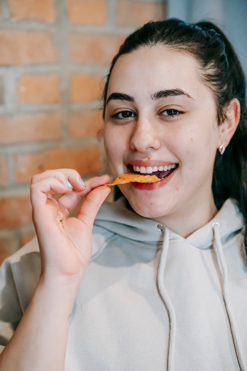 A woman smiles as she crunches down on a chip.