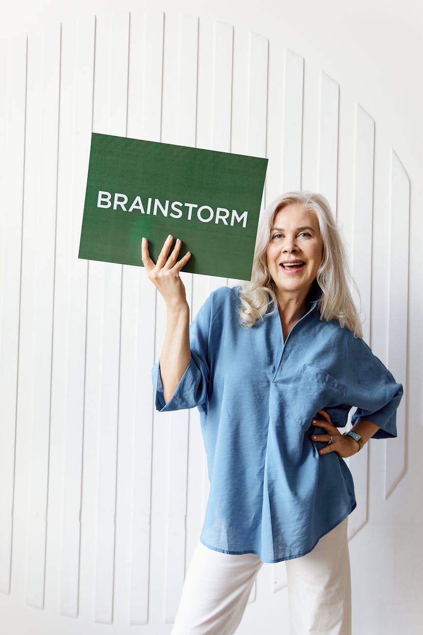 A woman in a blue shirt smiles and holds a sign saying, brainstorm.