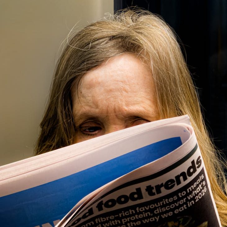 A woman's frown can be seen over the top of a newspaper that she is reading.
